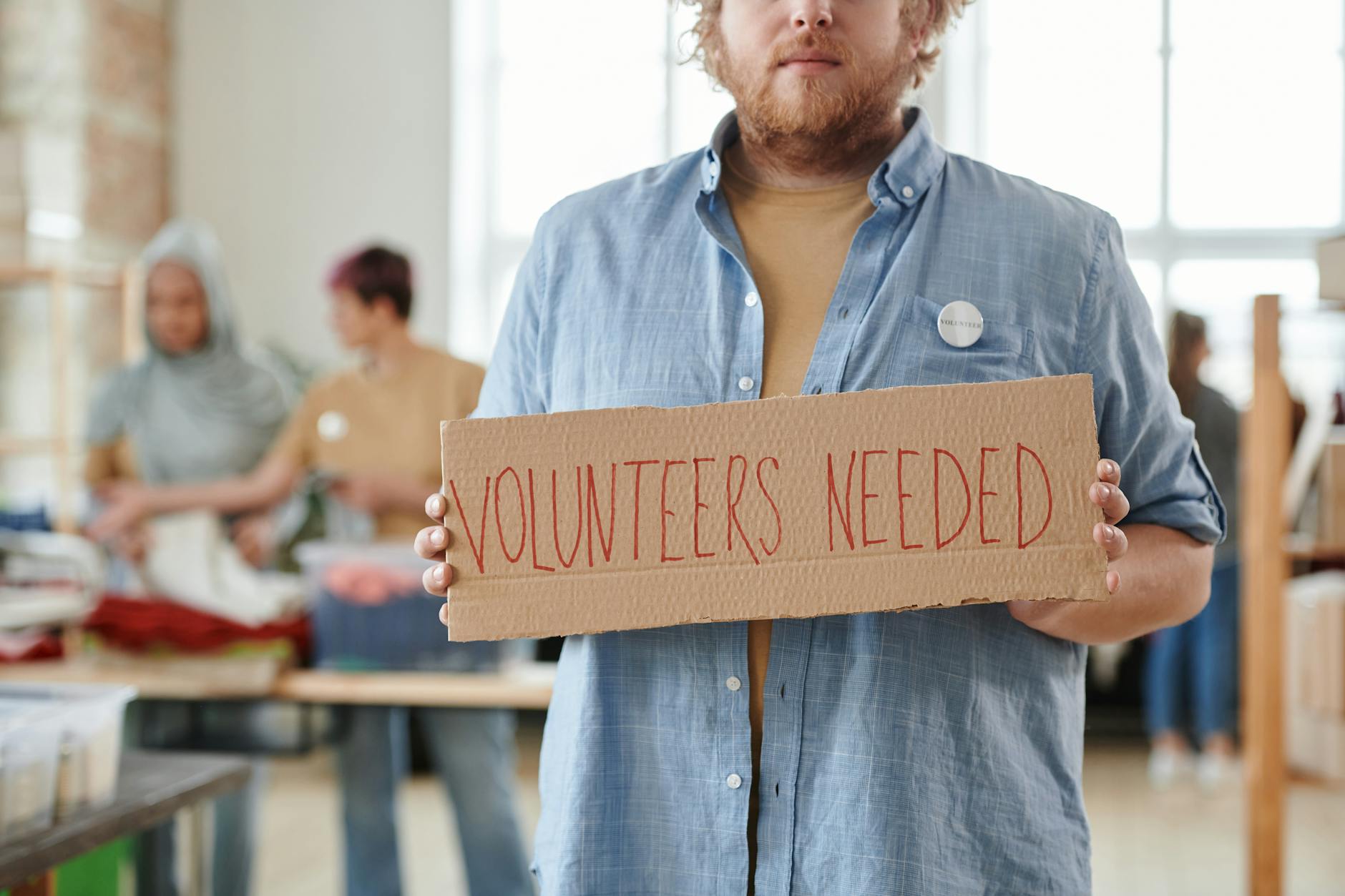 man holding a sign saying volunteers needed